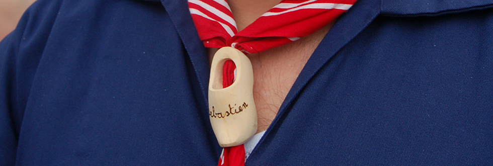 Een houten klompje als hanger, gegraveerd, aan een rood-witte halsdoek